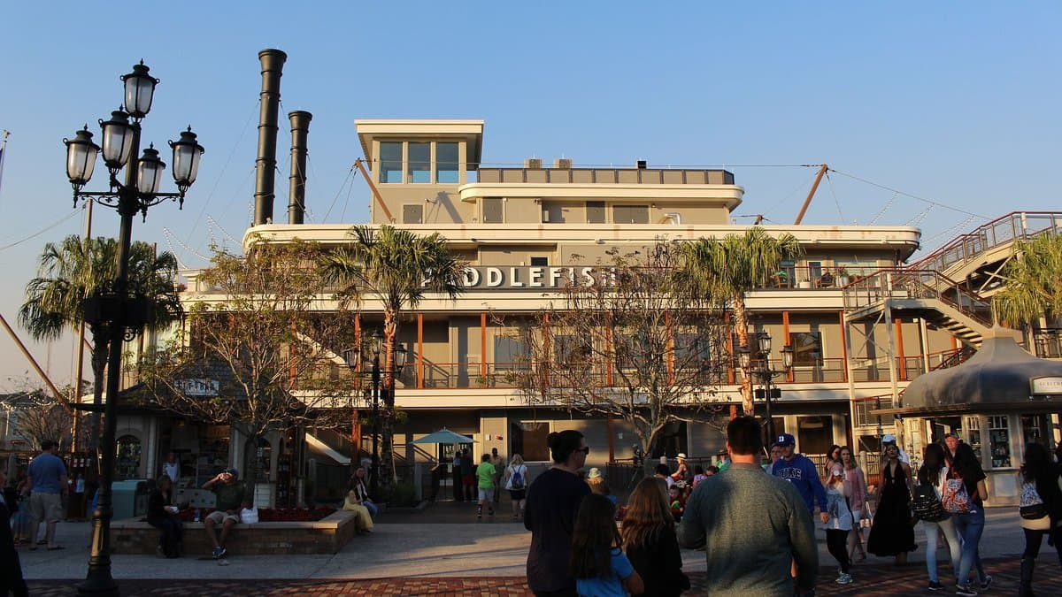 The multi-deck Paddlefish restaurant at Disney Springs permanently moored as a full-size paddlewheel riverboat, twin black smokestacks and the Paddlefish name rising above the waterfront promenade on a clear sunny afternoon.