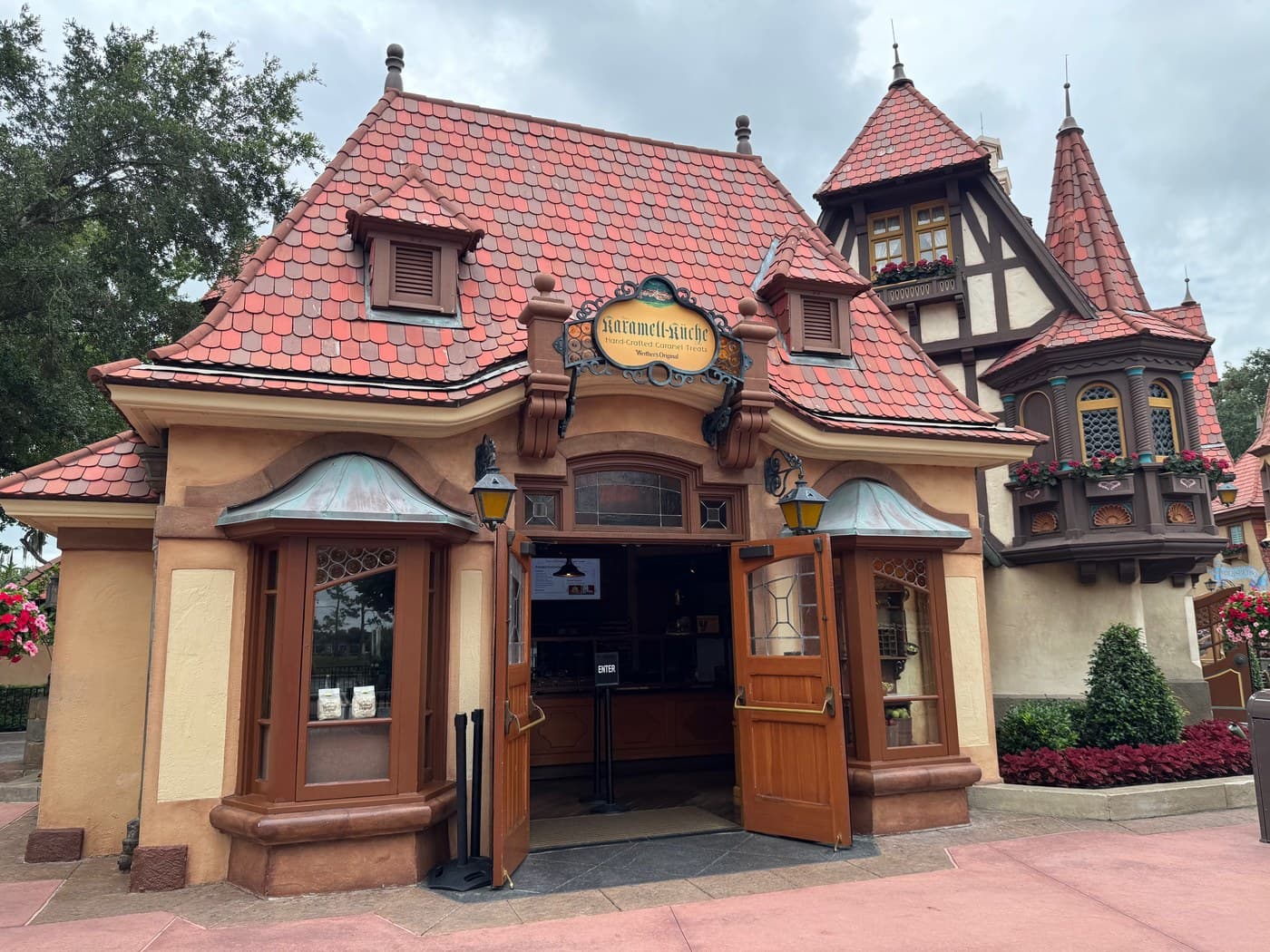 The front of Karamell-Küche in EPCOT's Germany pavilion: a small shop with a red tiled roof and its wooden doors open under a sign reading "Karamell-Küche, Hand-Crafted Caramel Treats, Werther's Original".