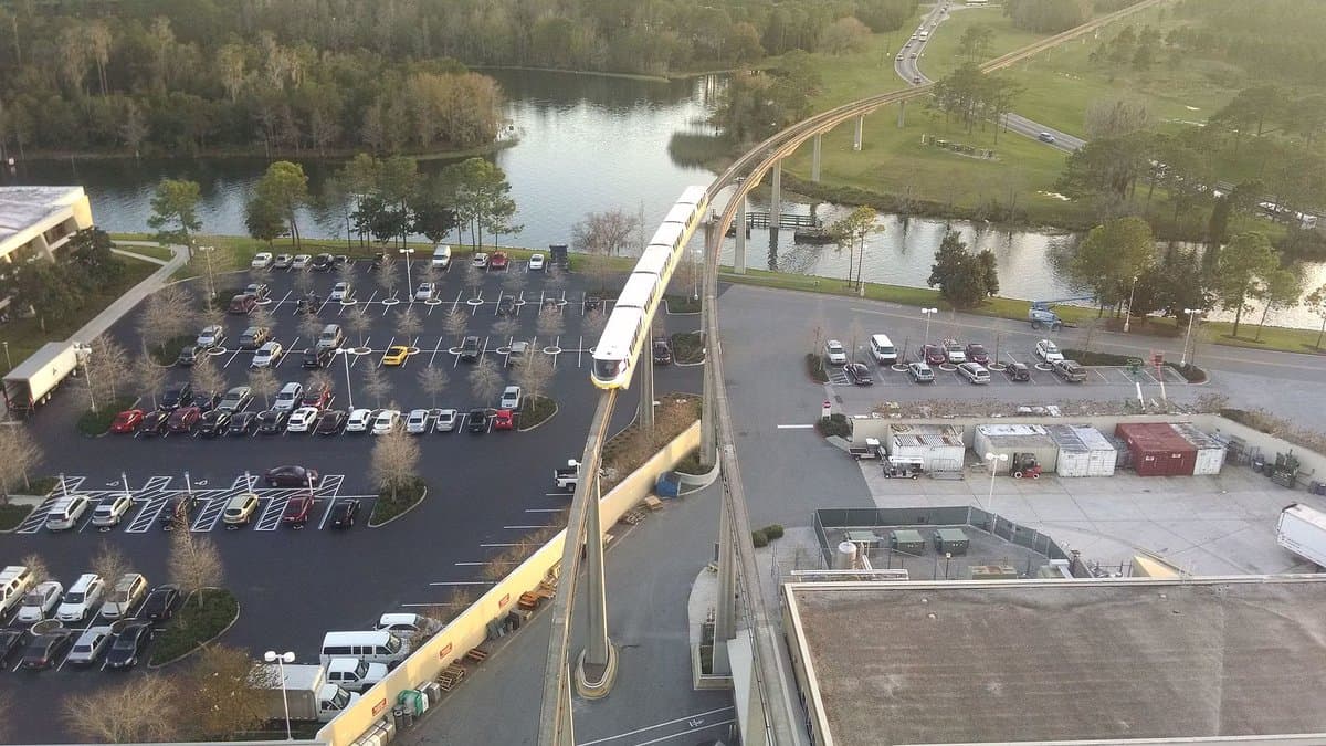 Aerial view from the top of Disney's Contemporary Resort, looking down on the Walt Disney World monorail curving away on its elevated beam above the resort and surrounding Florida woodlands — the same altitude where California Grill's rooftop dining room and its panoramic windows are located.