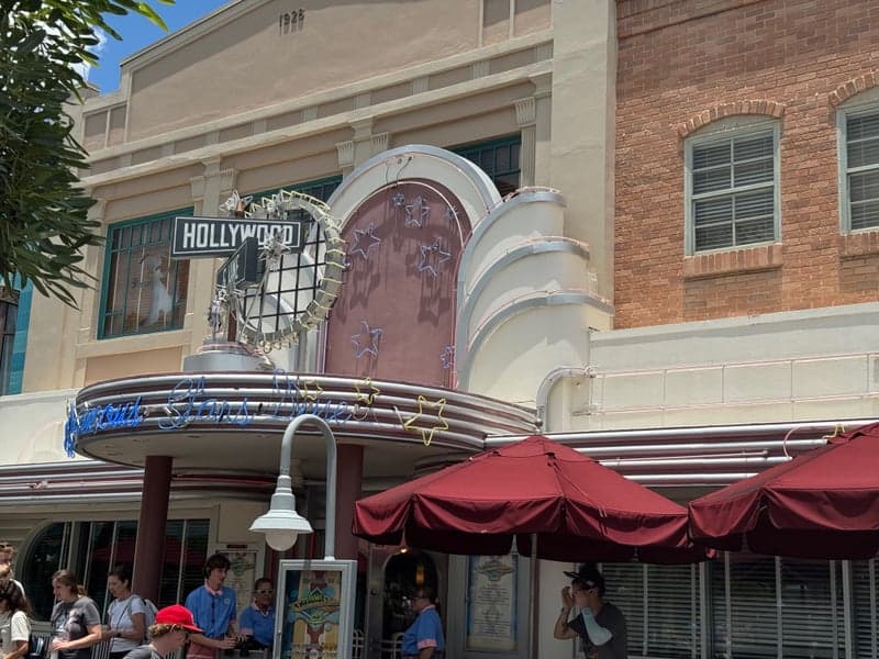 The neon-lit Art Deco marquee of Hollywood & Vine at Disney's Hollywood Studios — street-sign-style Hollywood & Vine placards, a starburst neon display, and the glowing blue-script tagline Where Famous Stars Dine arching across the canopy.